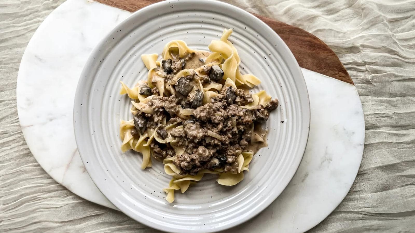 Plate of pasta topped with a creamy mushroom and ground meat sauce on a textured table surface.
