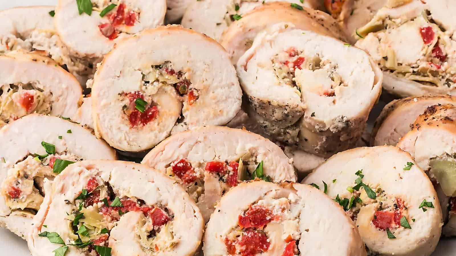 Sliced stuffed chicken breasts filled with cheese, herbs, and diced red peppers, garnished with chopped parsley.