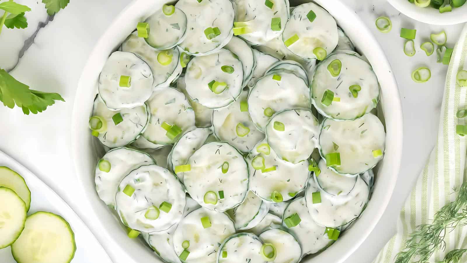 A bowl of cucumber slices mixed with creamy dressing and garnished with chopped green onions.