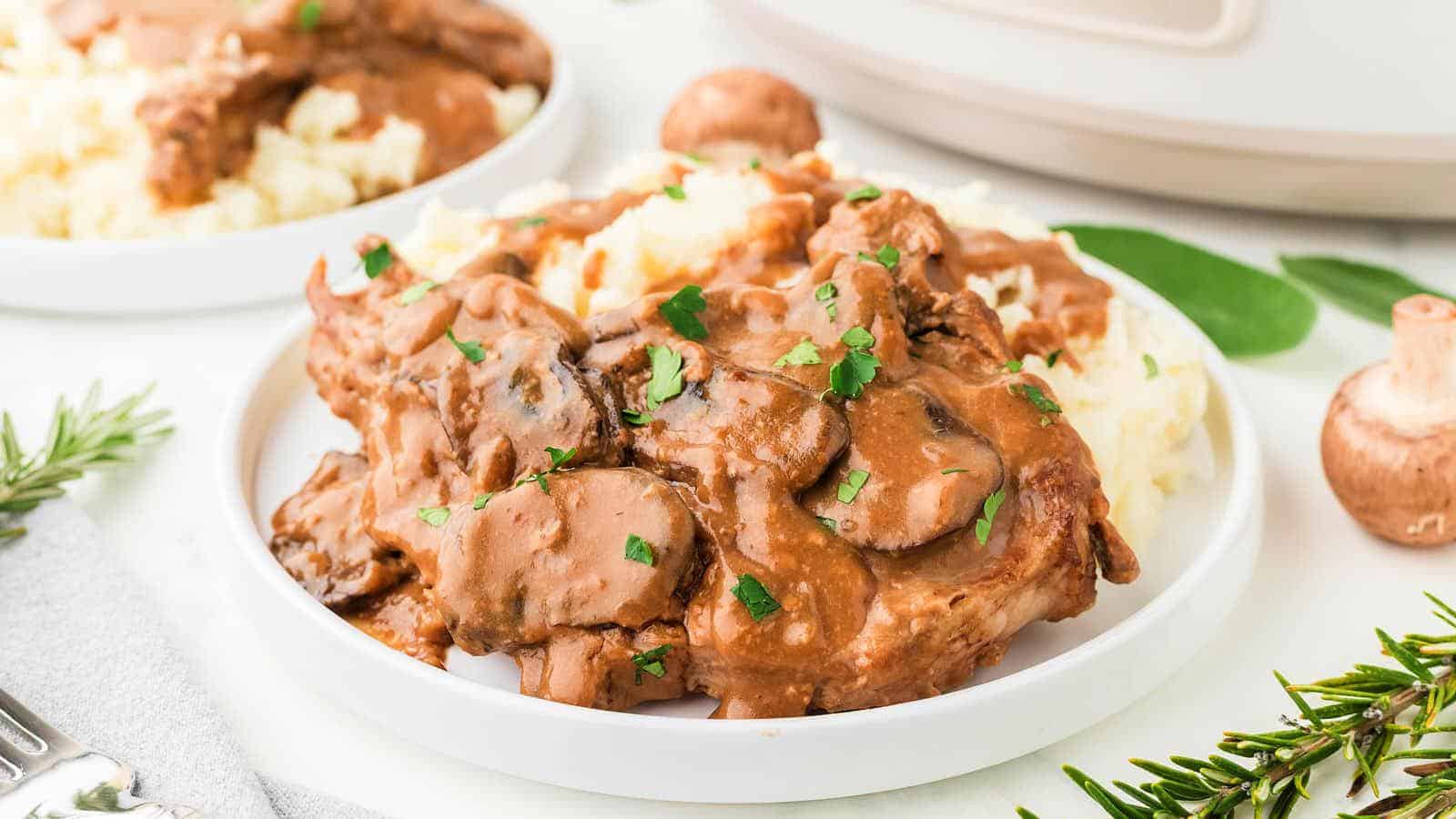 A plate of mashed potatoes topped with beef and mushroom gravy, garnished with chopped herbs.
