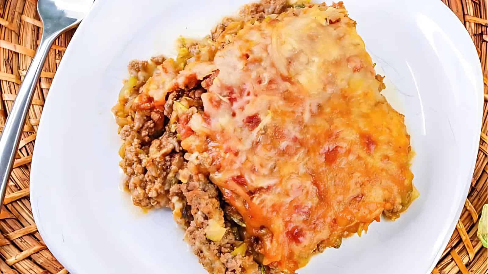 A serving of cheesy baked casserole with ground meat, vegetables, and tomato sauce on a white plate.