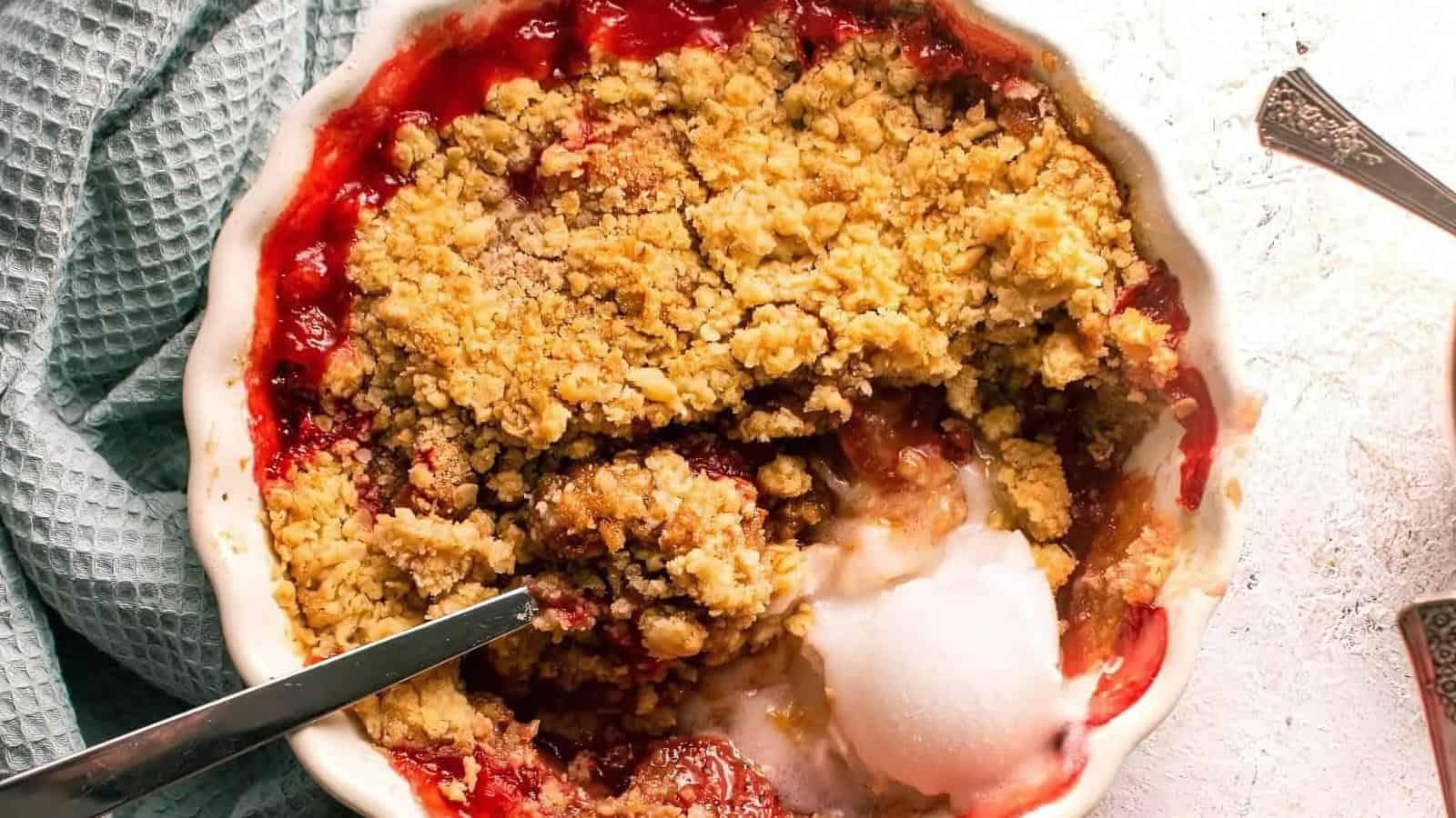 A dish of fruit crumble with a golden crumb topping, a portion served out, and a scoop of melting vanilla ice cream beside it.