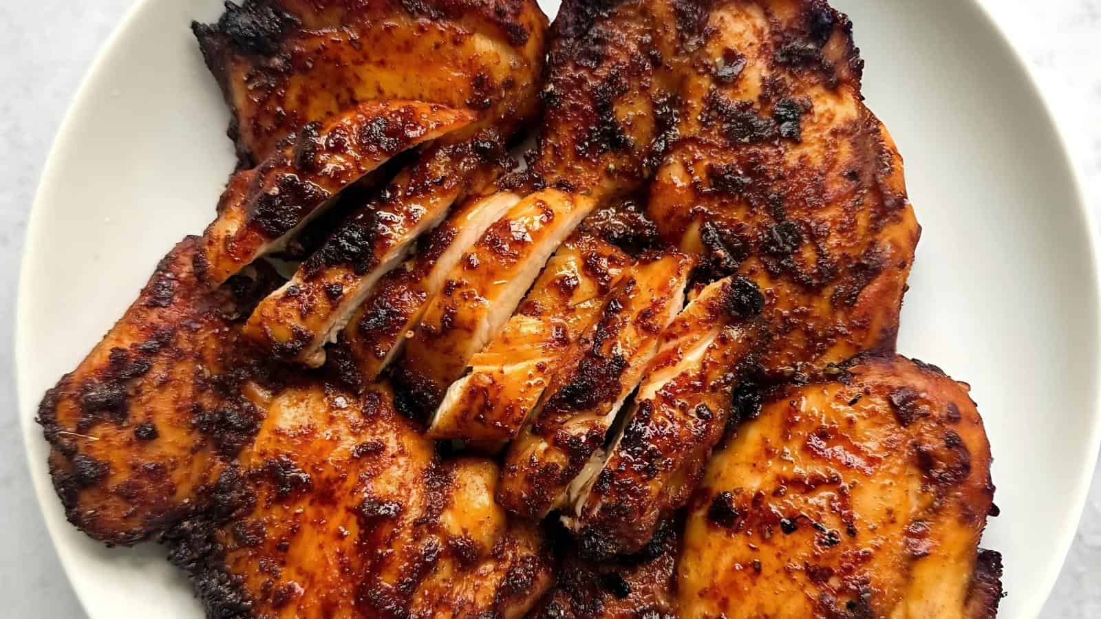 Grilled chicken breasts, some whole and some sliced, arranged on a white plate.