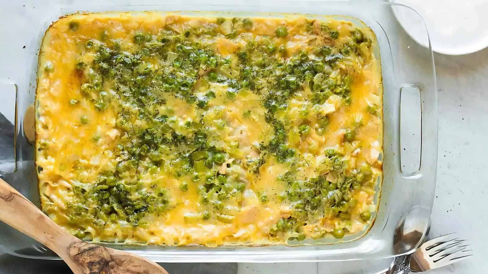 A glass baking dish filled with a baked casserole topped with melted cheese and chopped green herbs or vegetables.