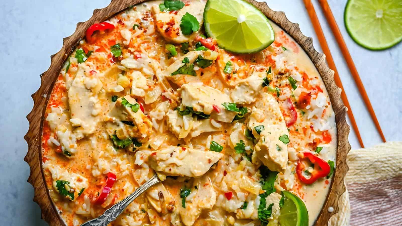 A bowl of creamy chicken and rice soup garnished with cilantro, sliced red chili, and lime wedges; chopsticks and a napkin are beside the bowl.