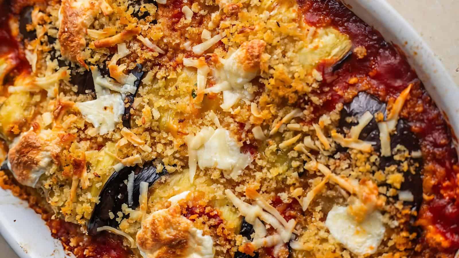 Close-up of a baked dish featuring layers of sliced eggplant, tomato sauce, melted cheese, and a golden breadcrumb topping.