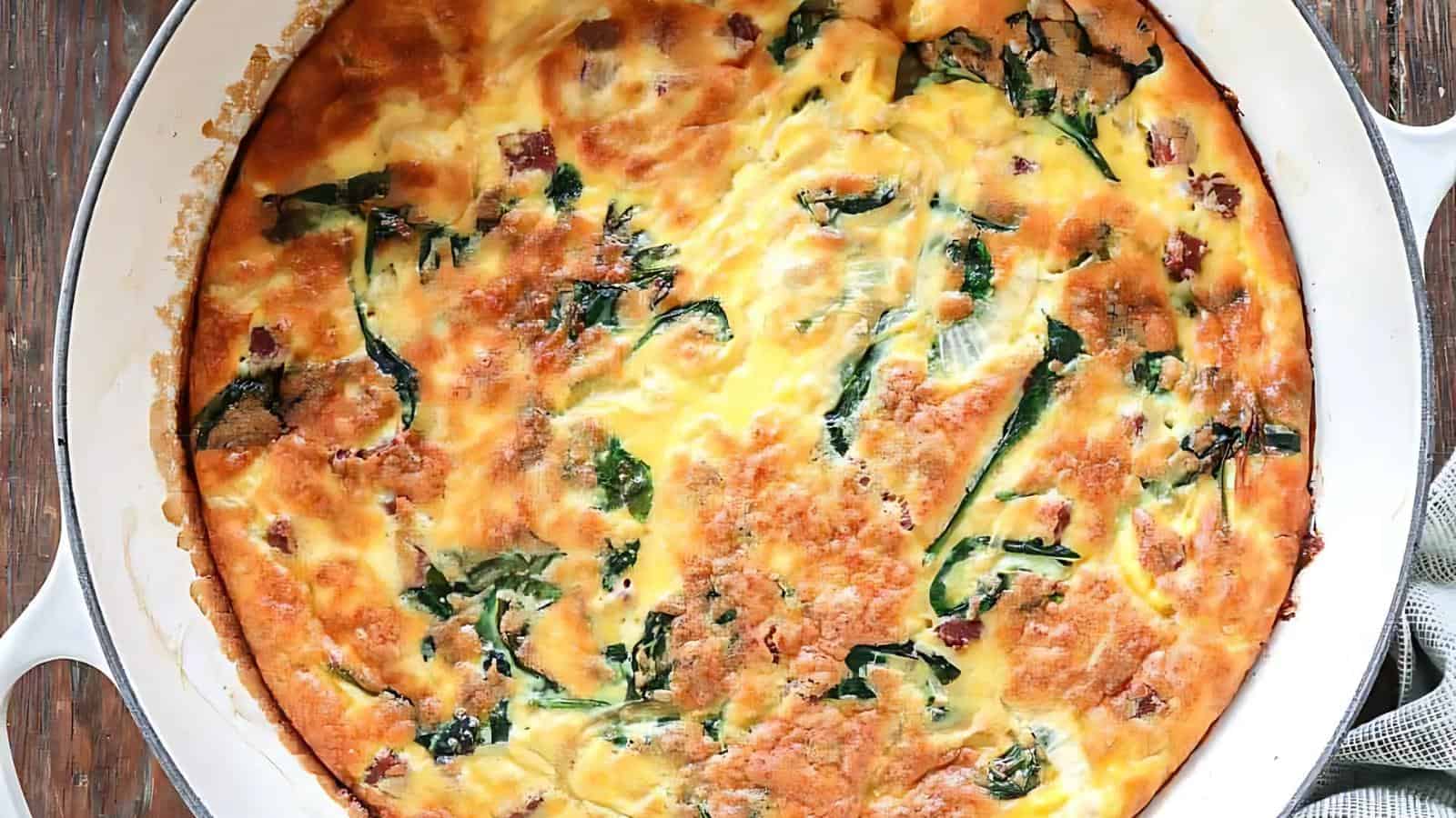 A baked frittata in a white dish, featuring a golden crust with visible spinach and melted cheese.