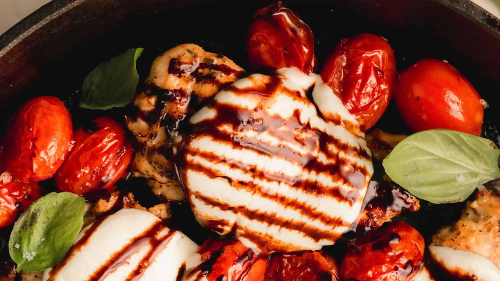 Grilled chicken topped with melted mozzarella, roasted cherry tomatoes, fresh basil leaves, and a drizzle of balsamic glaze in a skillet.