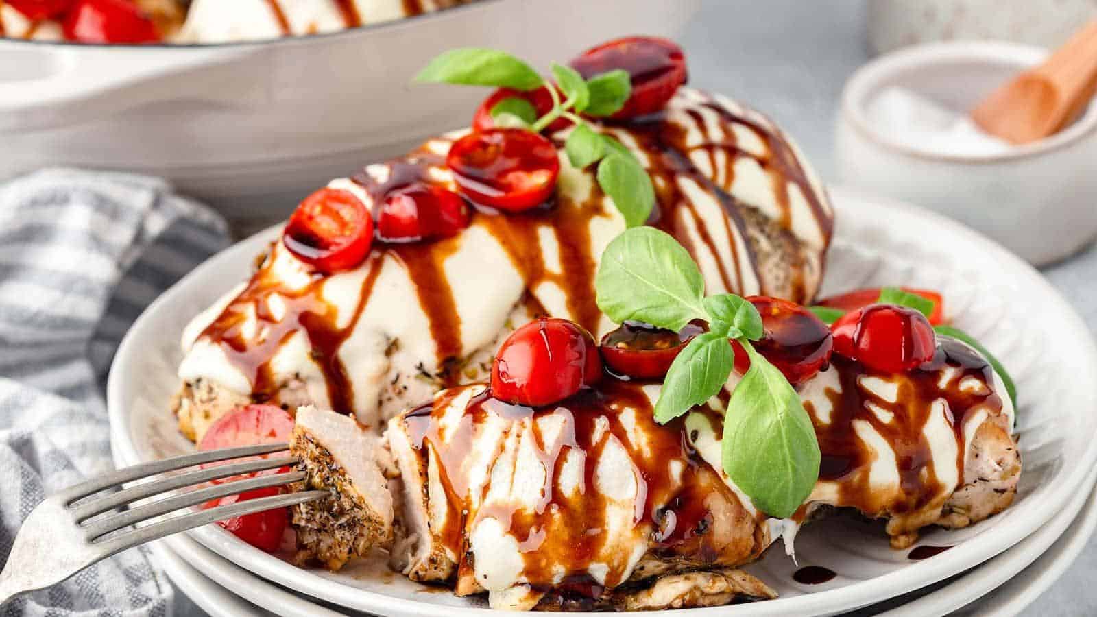 Grilled chicken breasts topped with mozzarella, cherry tomatoes, and fresh basil, drizzled with balsamic glaze on a white plate.