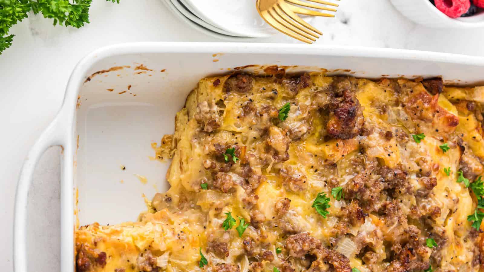 A baked casserole with cooked meat, melted cheese, and garnished with parsley in a white dish. A portion is missing from one corner.