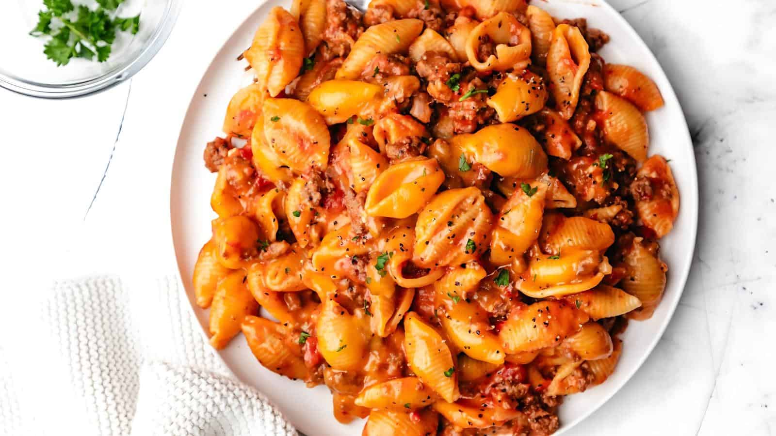 A plate of pasta with shell noodles, minced meat, and a tomato-based sauce, garnished with chopped parsley.