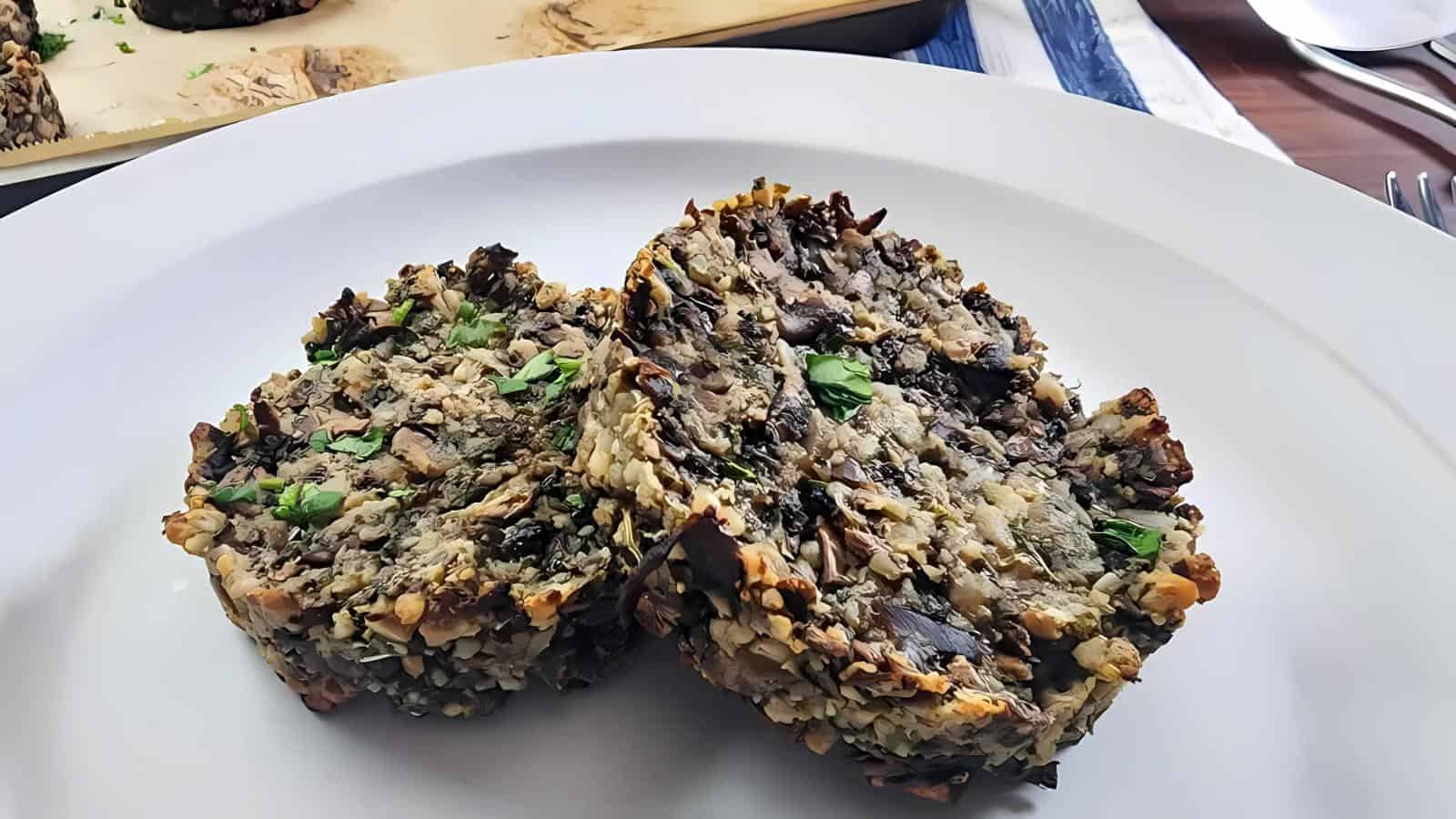 Two slices of a nut and mushroom loaf served on a white plate, garnished with chopped herbs.