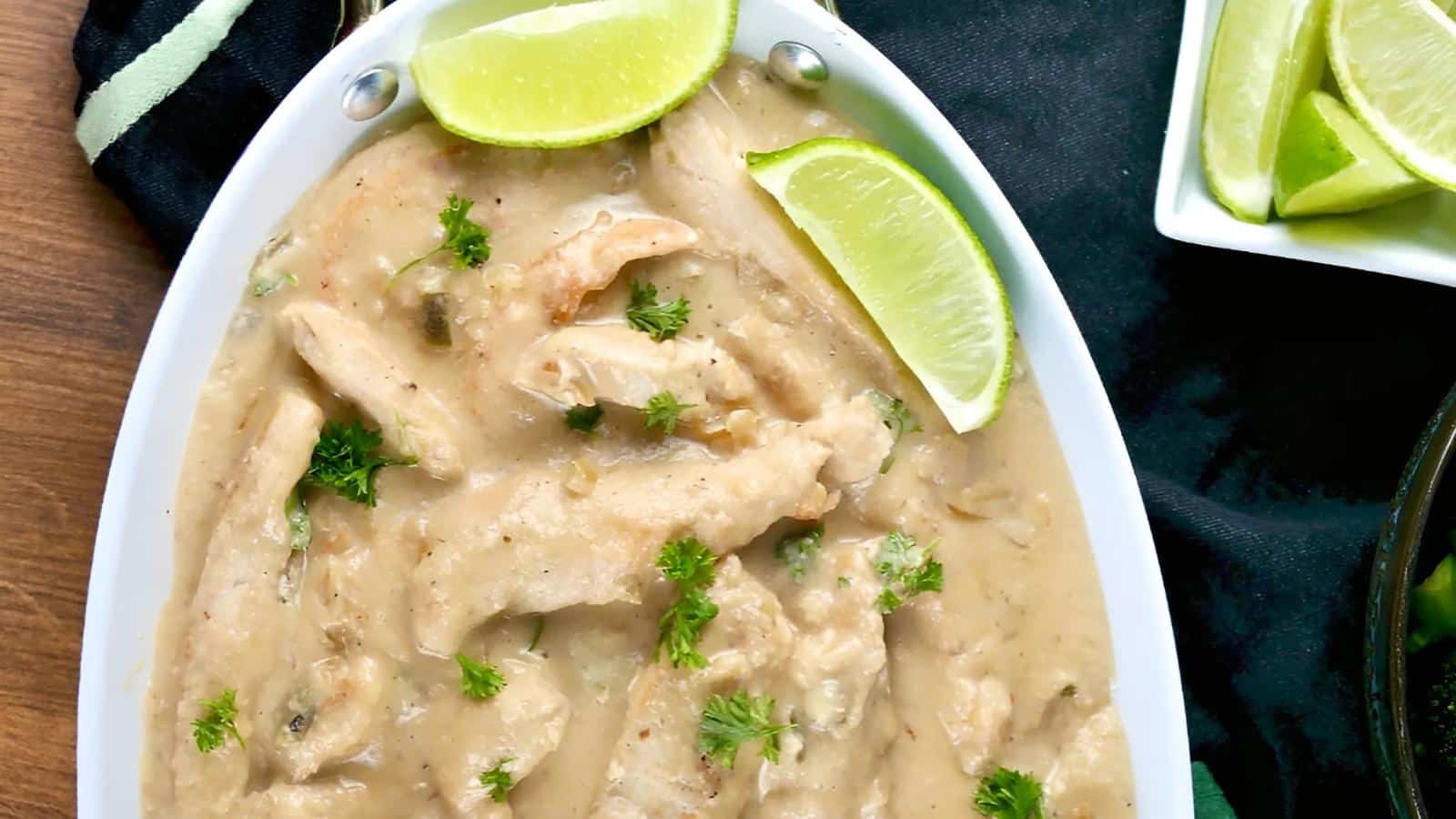 Oval dish filled with creamy chicken strips garnished with fresh parsley and lime wedges, with extra lime slices on the side.