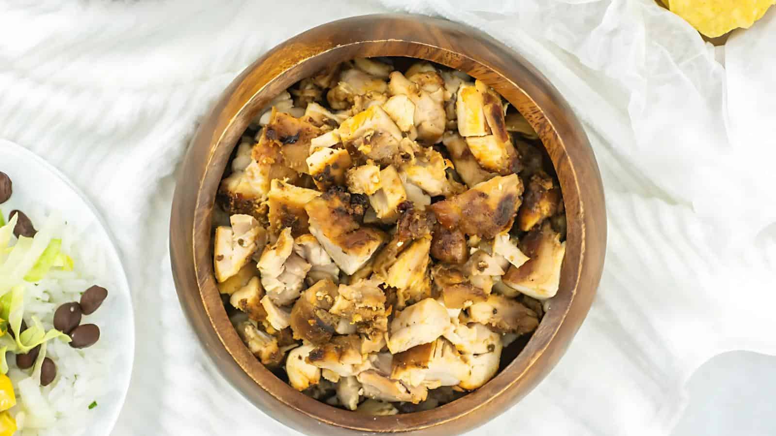 A wooden bowl filled with chopped, cooked chicken pieces on a white surface.