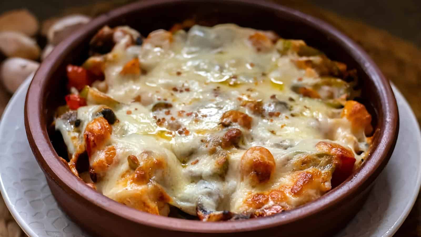 A baked dish in a brown ceramic bowl, topped with melted cheese and visible pieces of vegetables in a tomato-based sauce.