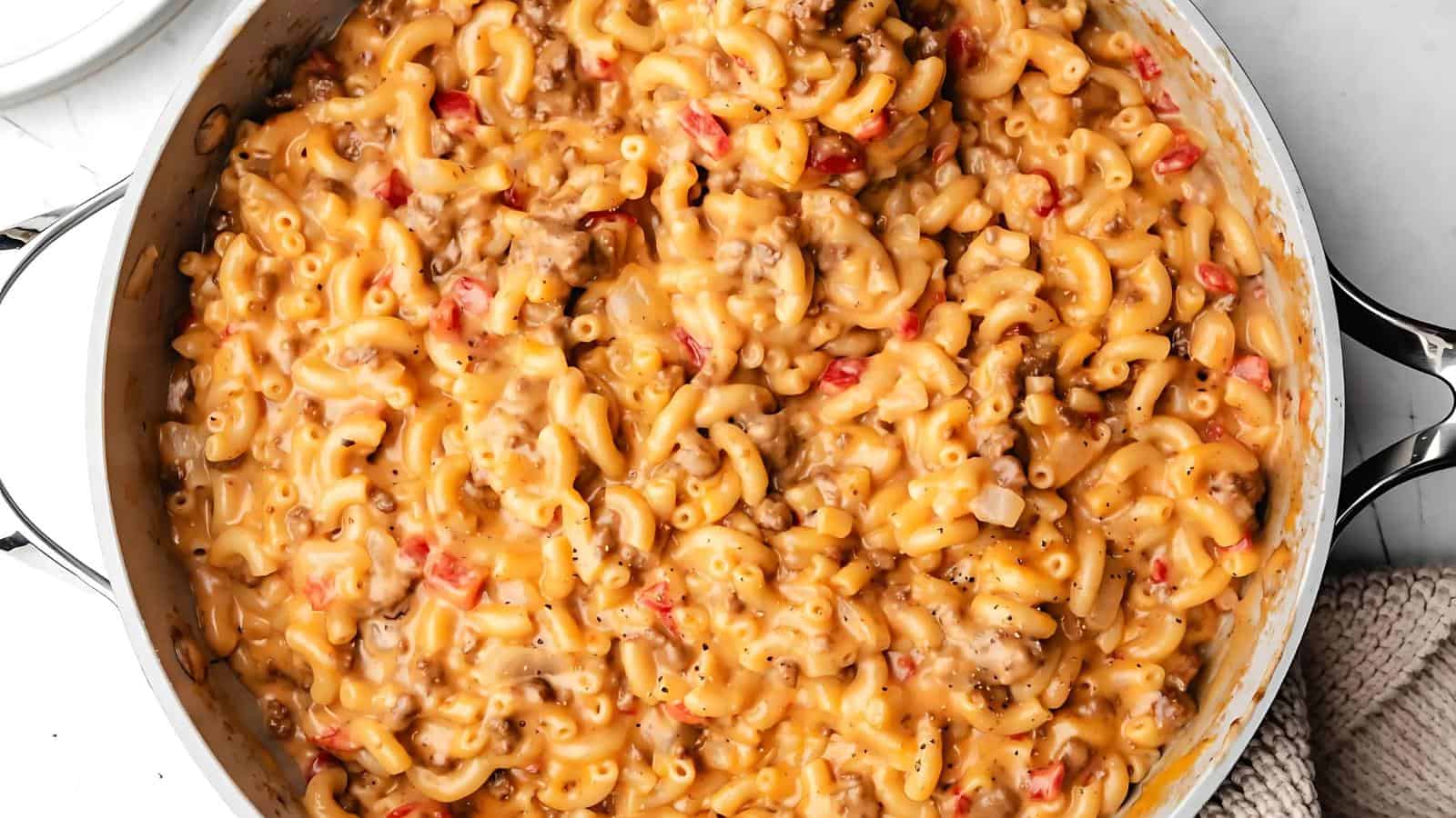 A pot of creamy macaroni and cheese mixed with ground meat and diced tomatoes.