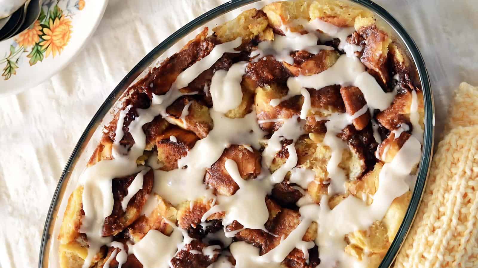 Oval dish with baked bread pudding topped with white icing drizzle, placed on a marble surface.