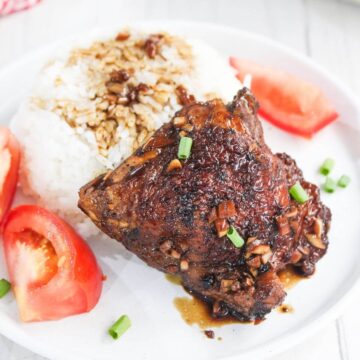 A plate with grilled chicken topped with sauce and chopped green onions, white rice, and sliced tomatoes.