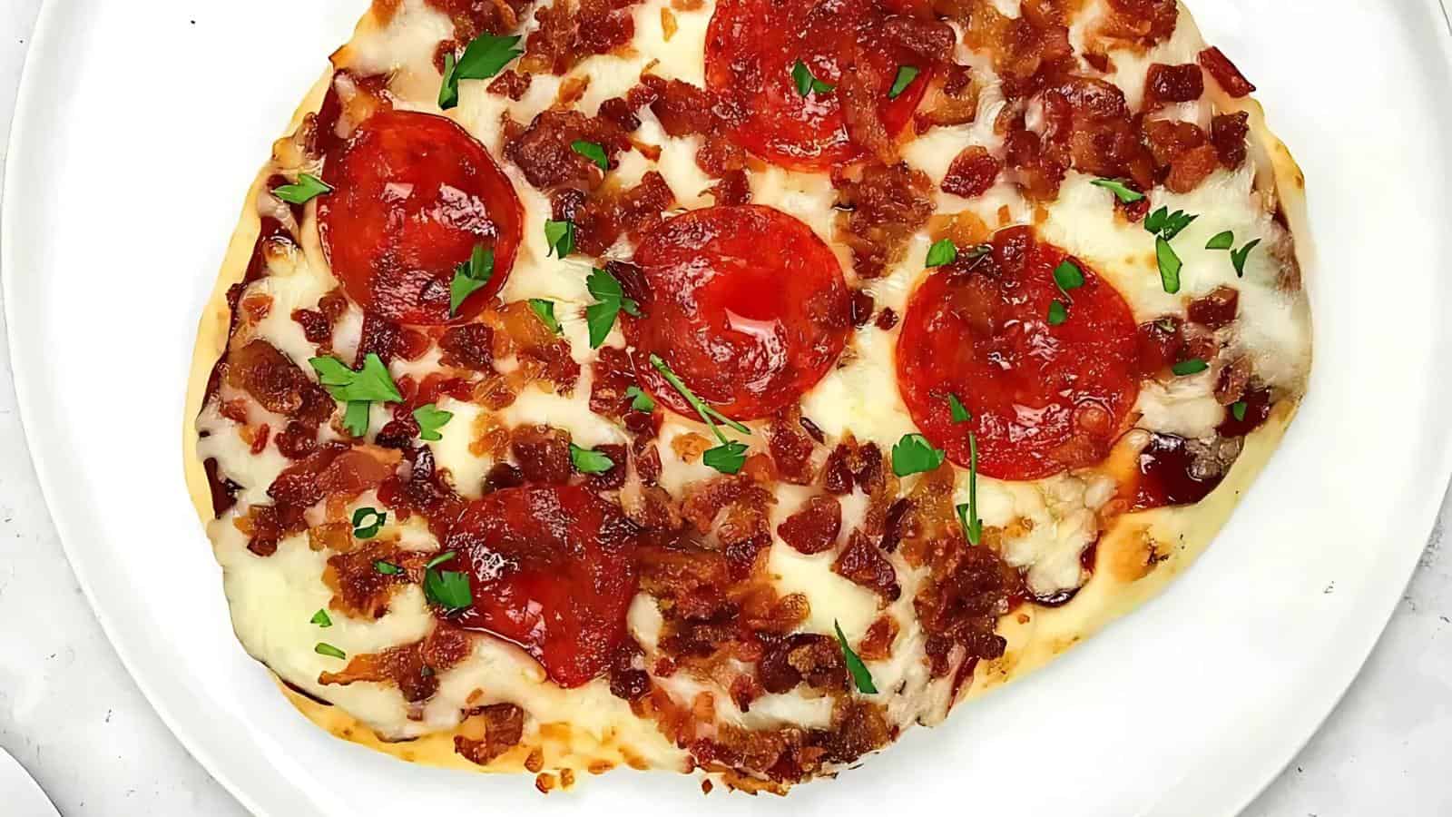 Personal-sized pizza topped with melted cheese, pepperoni slices, bacon bits, and chopped parsley on a white plate.