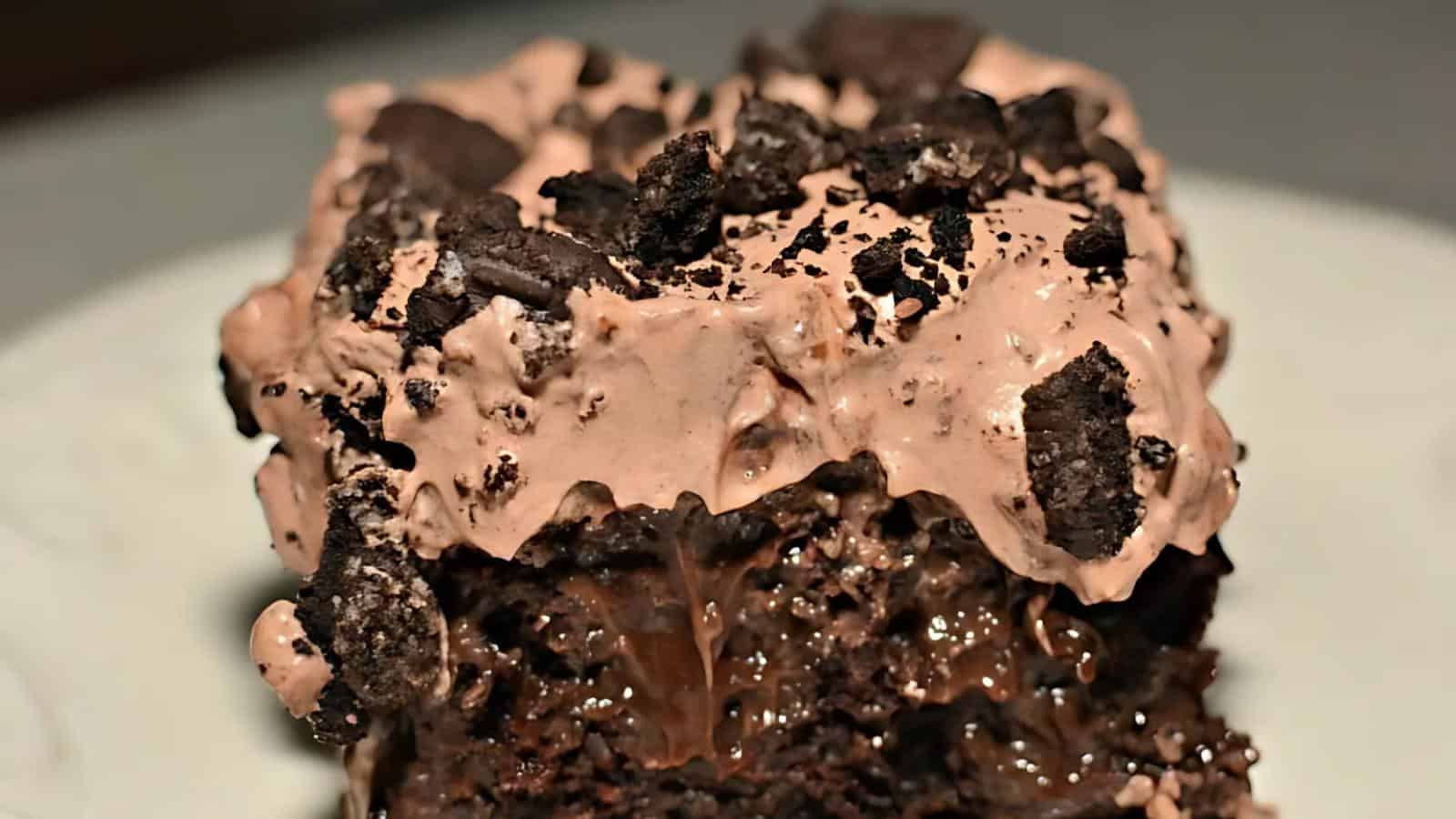 Close-up of a chocolate cake topped with chocolate cream and crushed cookies, with melted chocolate oozing from the center.