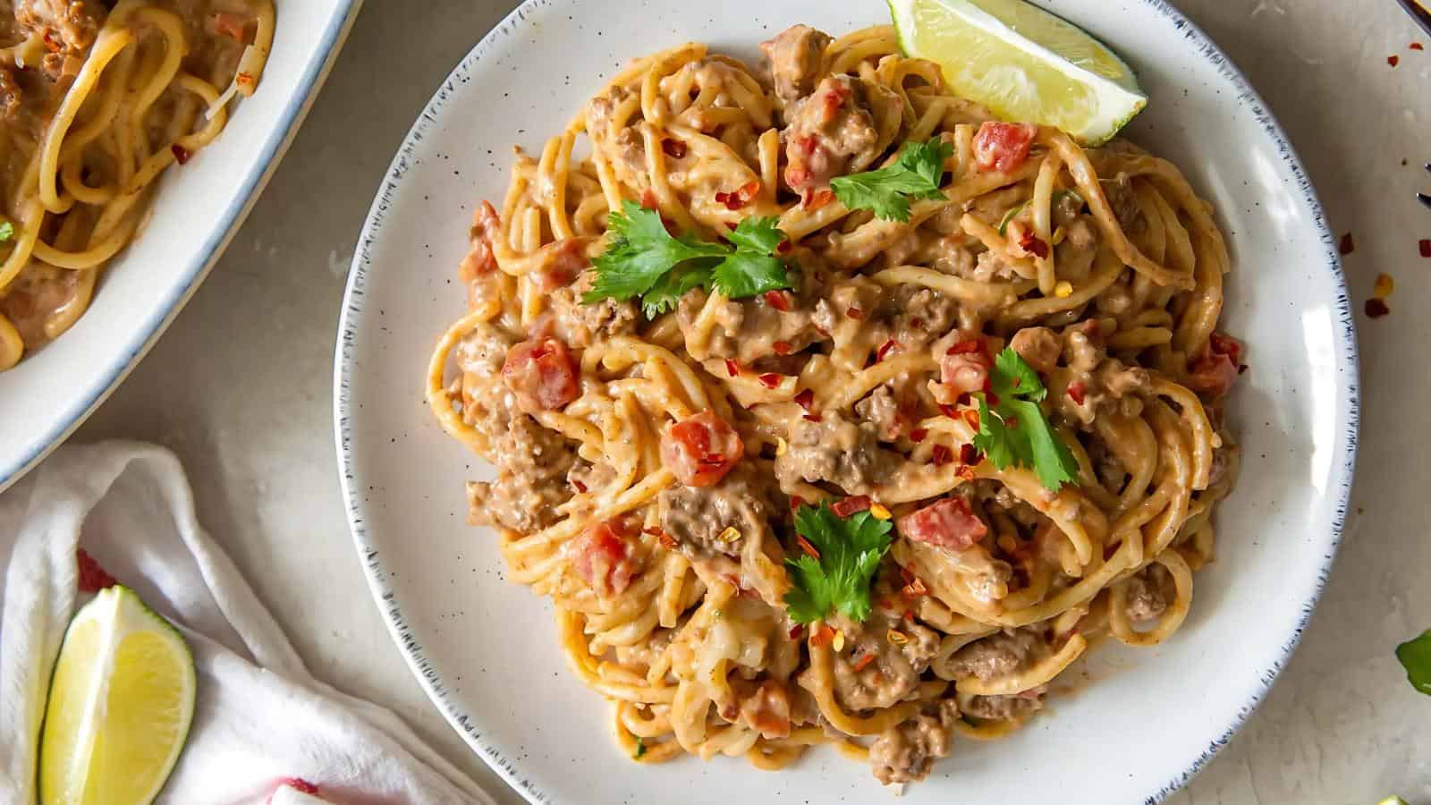 A plate of creamy spaghetti with ground meat, diced tomatoes, fresh cilantro, and a lime wedge on the side.