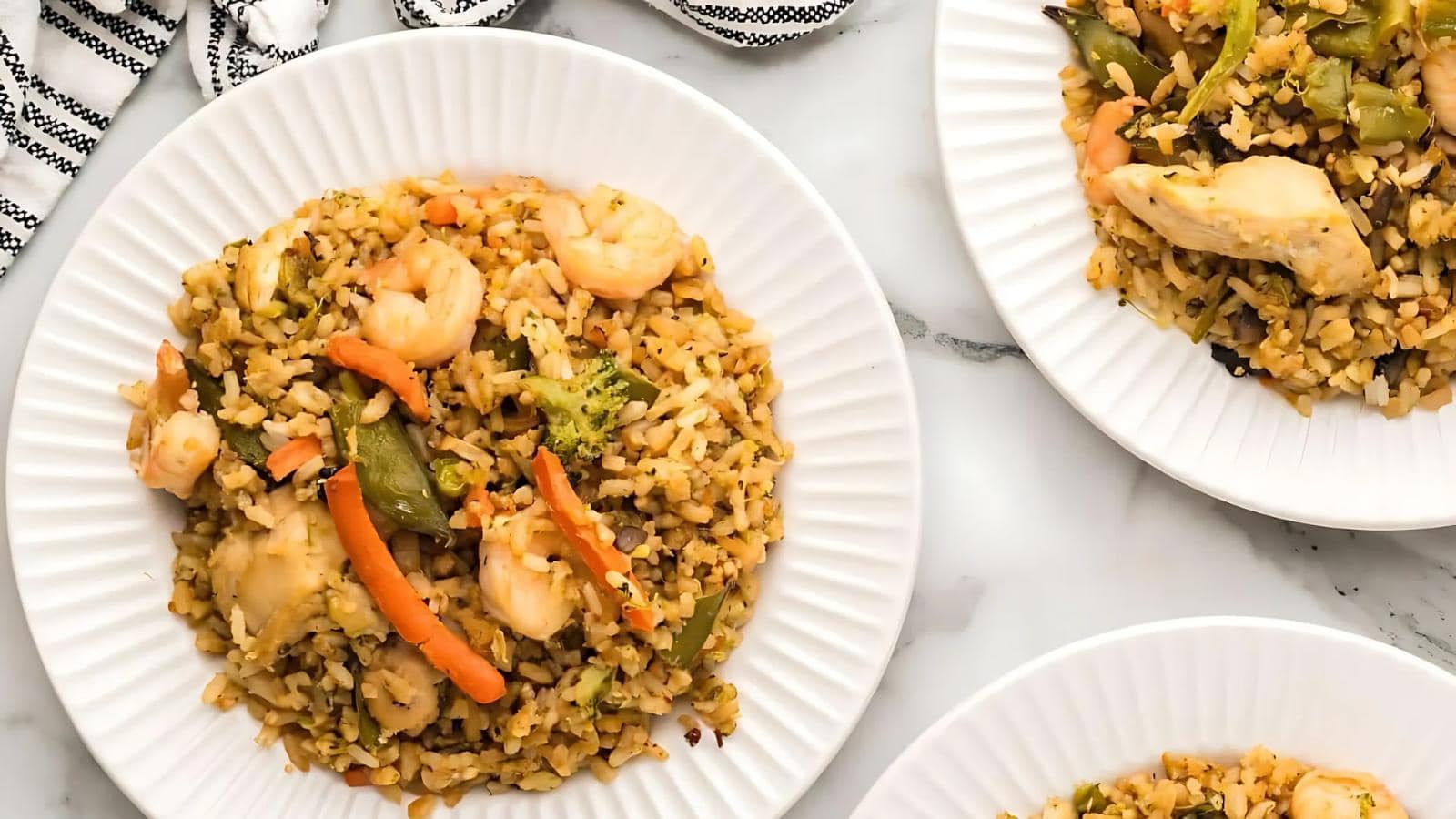 Three white plates with rice, shrimp, chicken, and mixed vegetables including carrots, broccoli, and snap peas, arranged on a white surface.