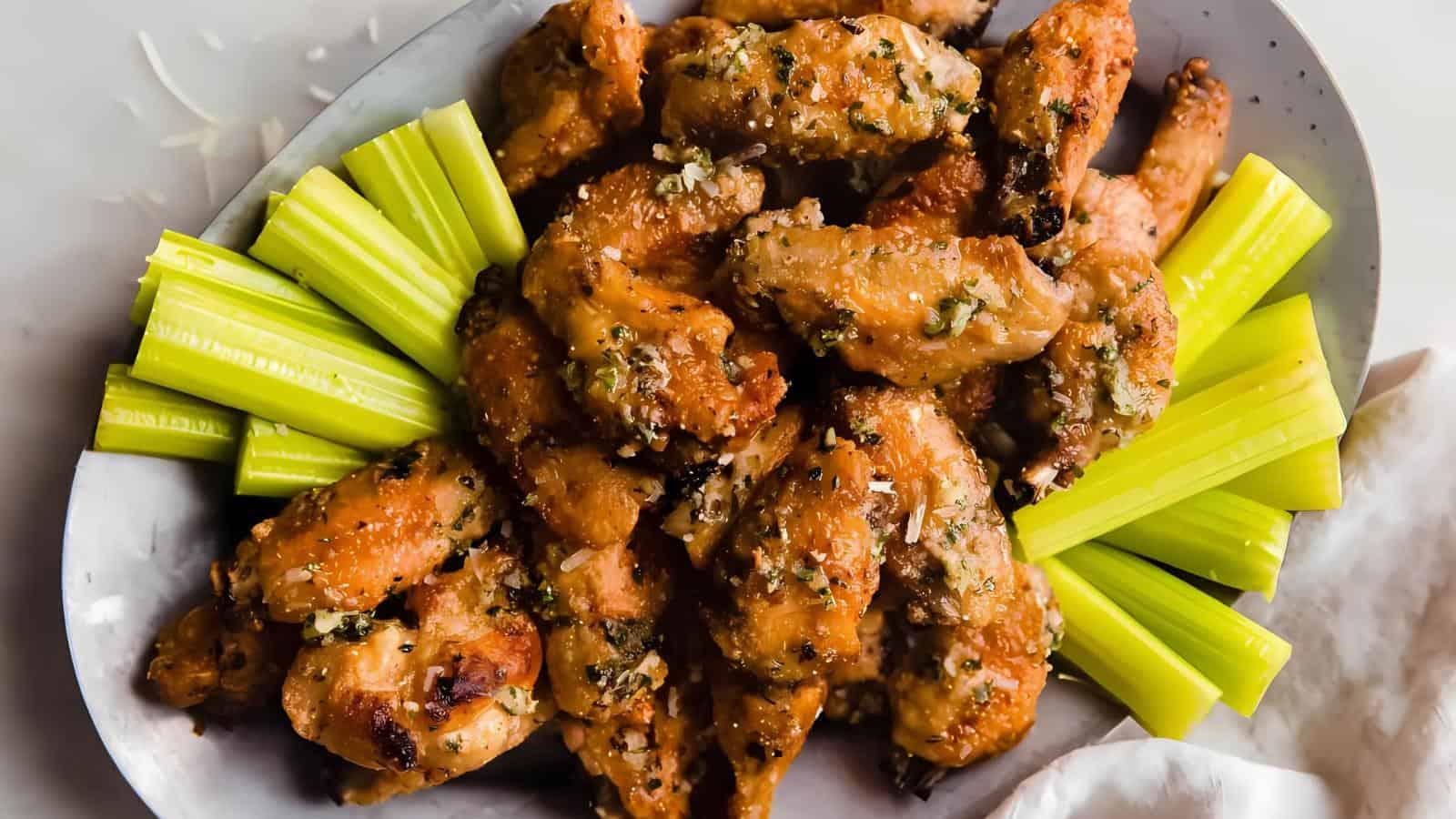 A plate of seasoned chicken wings is served with celery sticks, arranged neatly around the edges.