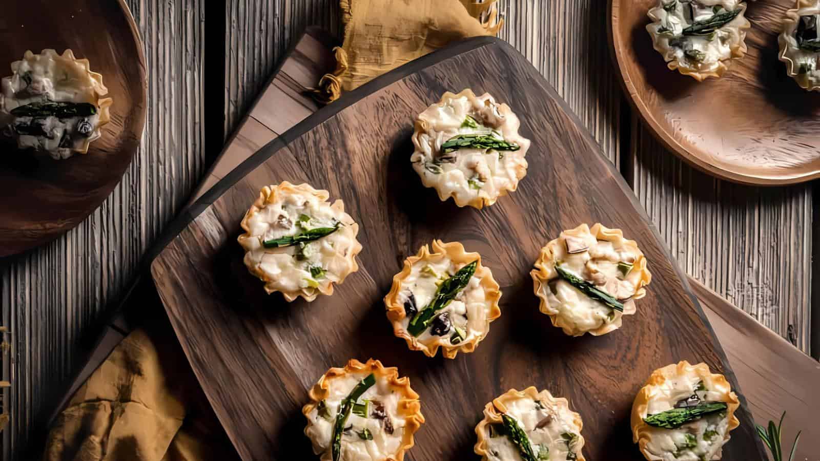Mini phyllo pastry cups filled with creamy mushroom and asparagus mixture arranged on a wooden board and plates.