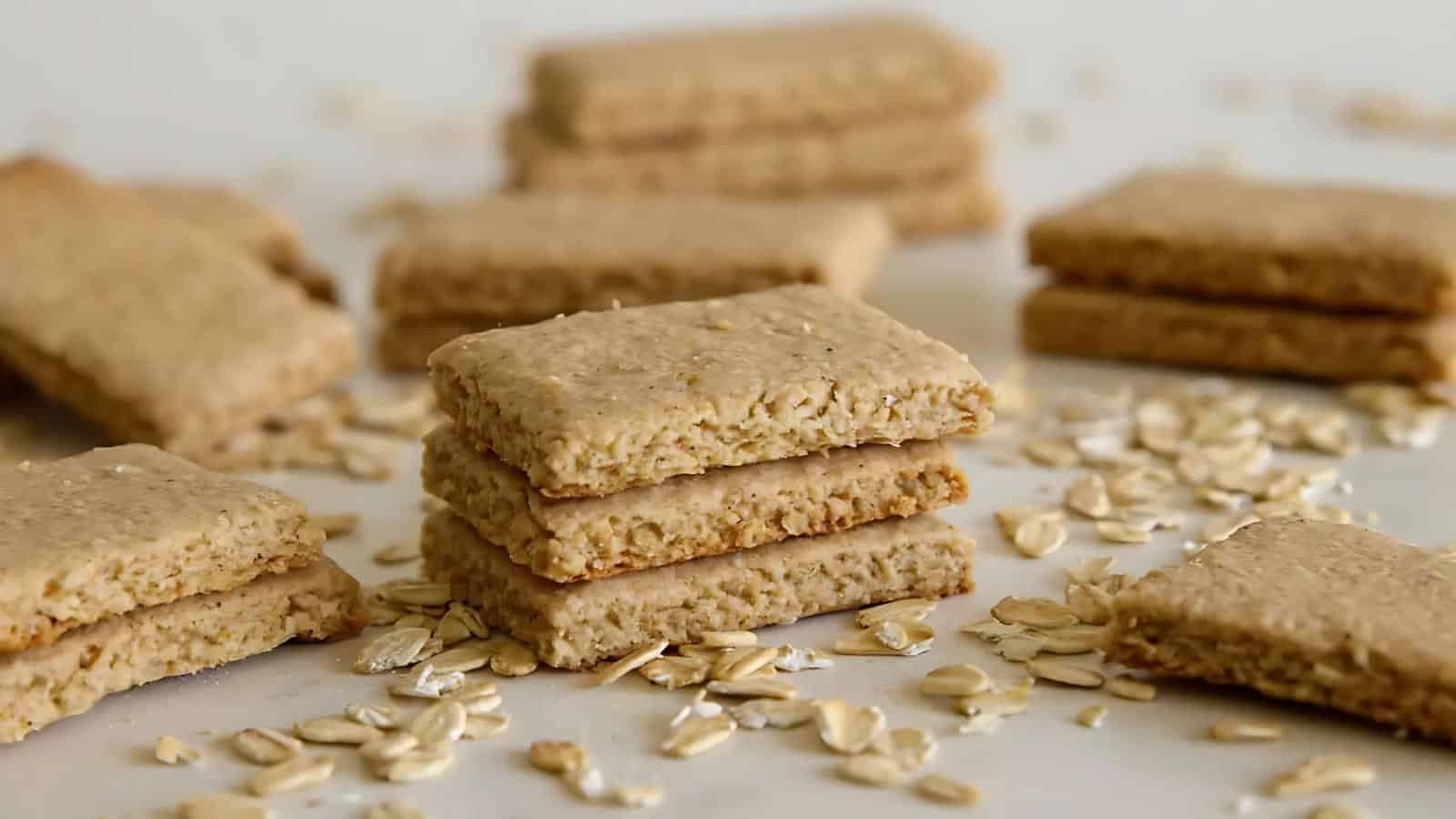 Stacks of rectangular oat biscuits are arranged on a white surface, surrounded by scattered rolled oats.