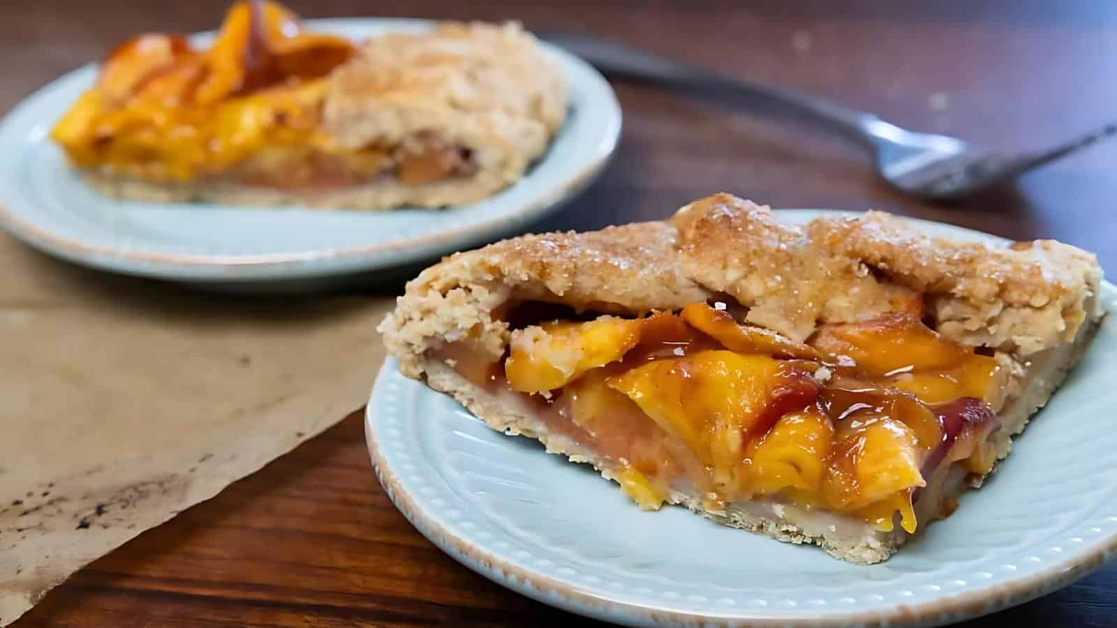 A close-up of a slice of peach pie on a blue plate, with another slice in the background and a fork on the table.