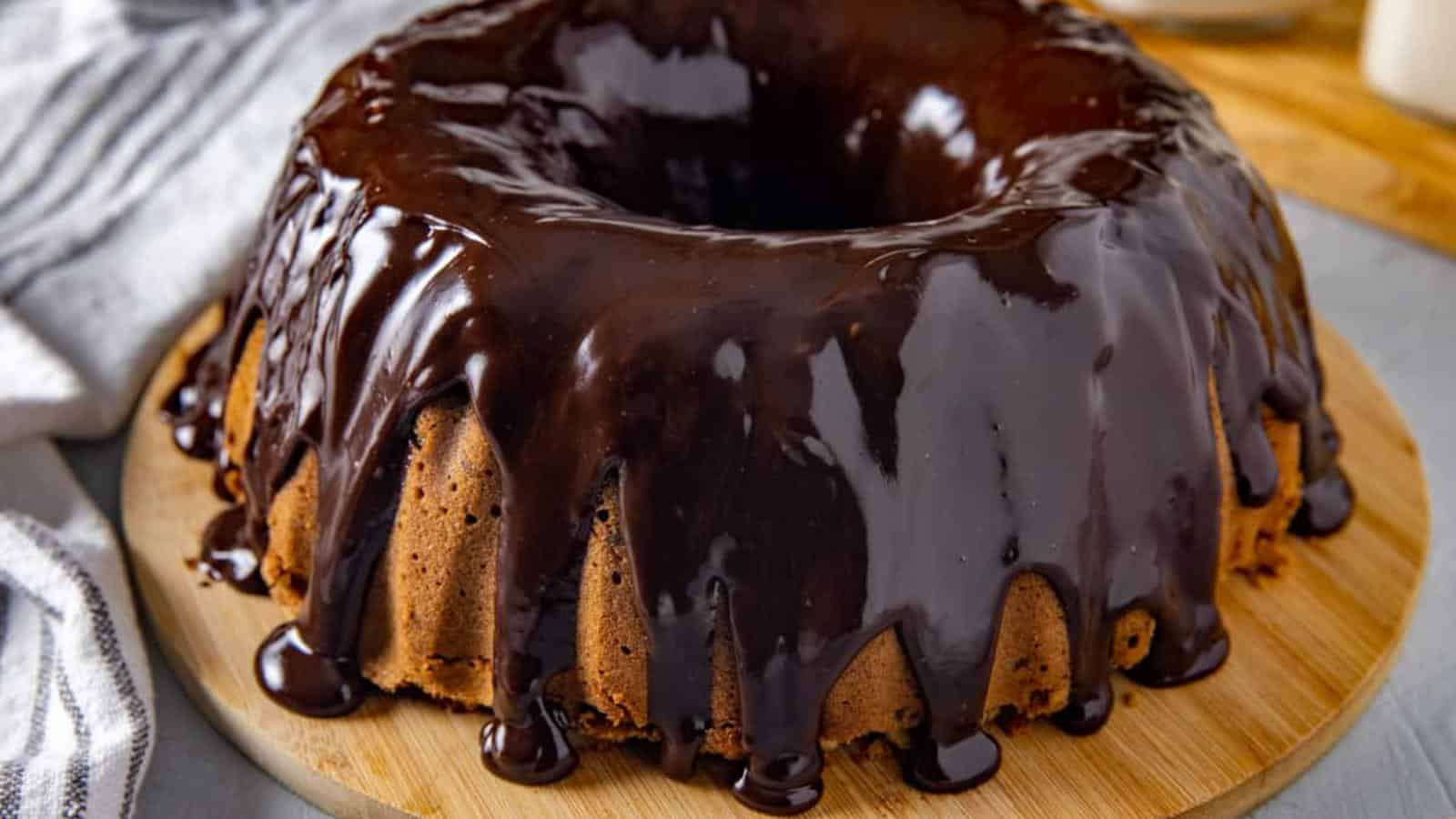 A bundt cake topped with glossy chocolate glaze sits on a wooden board.