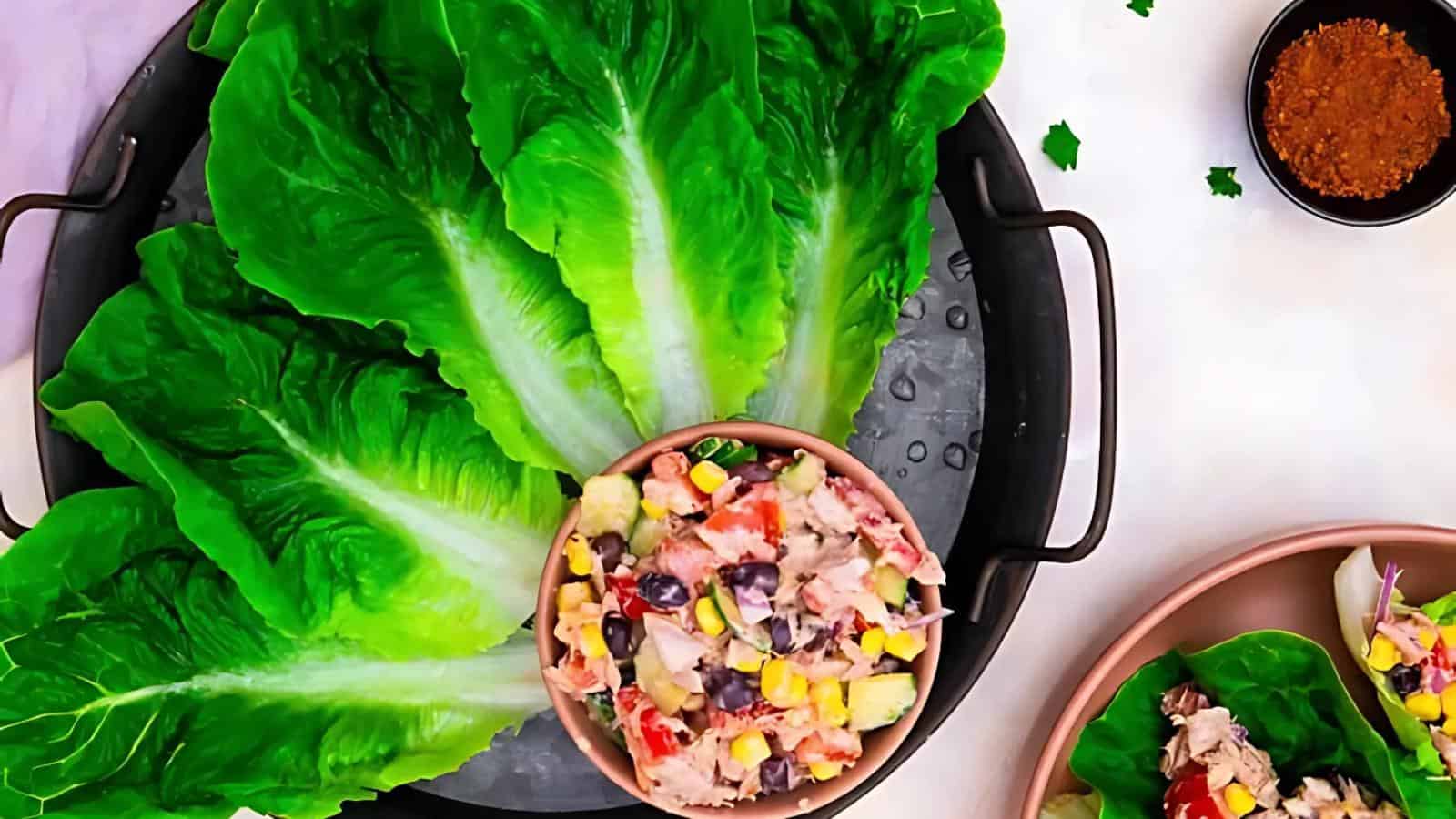 A tray with fresh romaine lettuce leaves, a bowl of mixed tuna salad with vegetables, and a small dish of seasoning on the side.