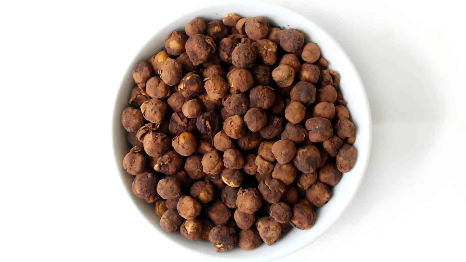 A white bowl filled with dried brown chickpeas on a white background.