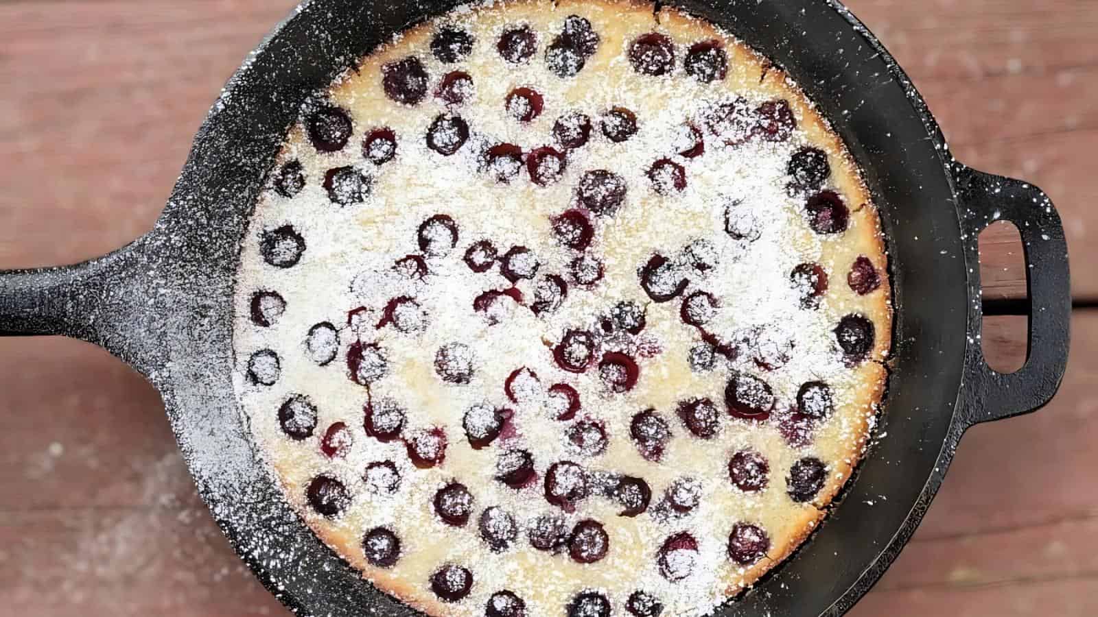 A baked cherry clafoutis dusted with powdered sugar in a black cast iron skillet, viewed from above.