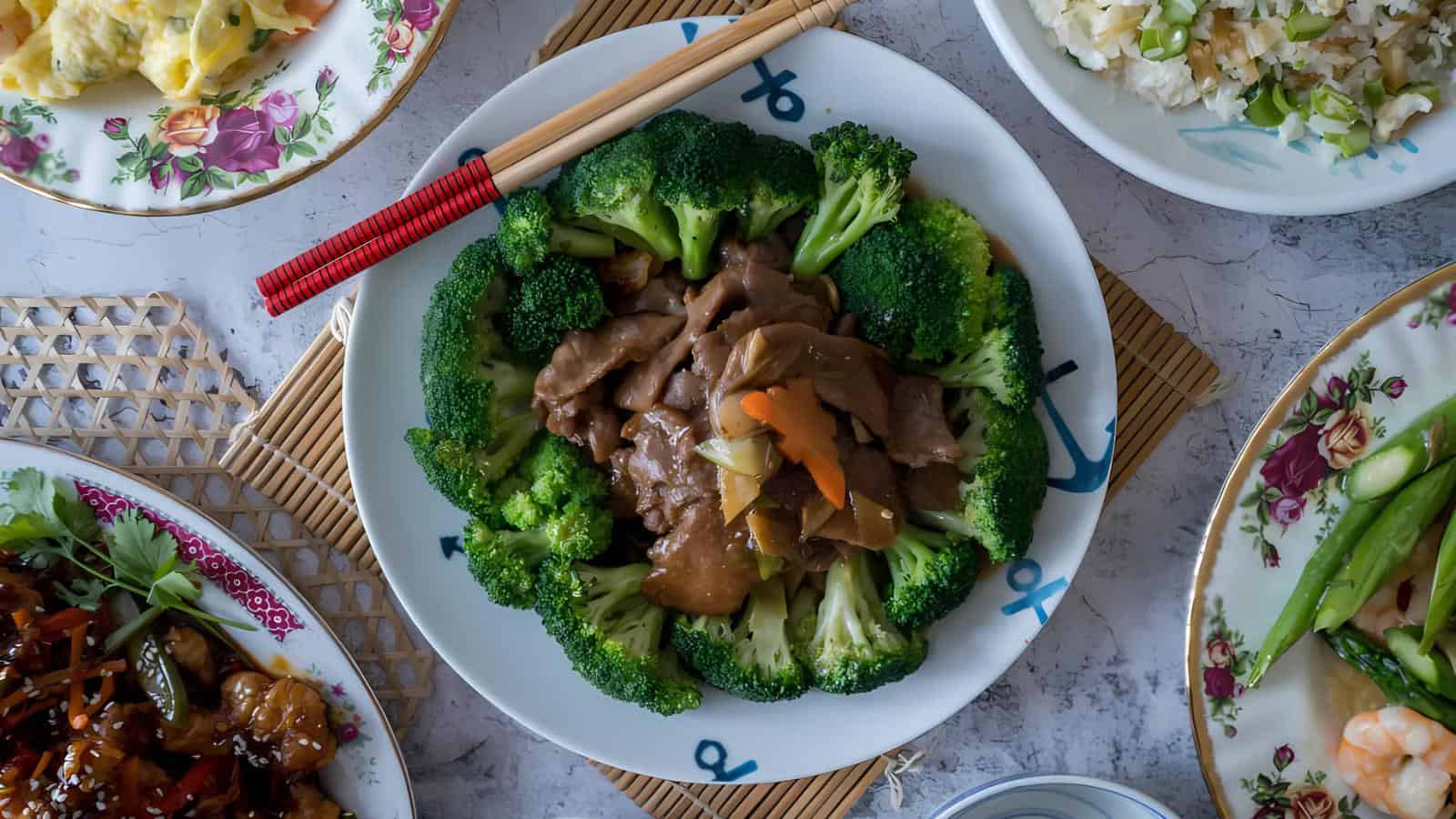 A plate of beef and broccoli stir-fry with brown sauce, surrounded by various side dishes and a pair of chopsticks resting on the plate.