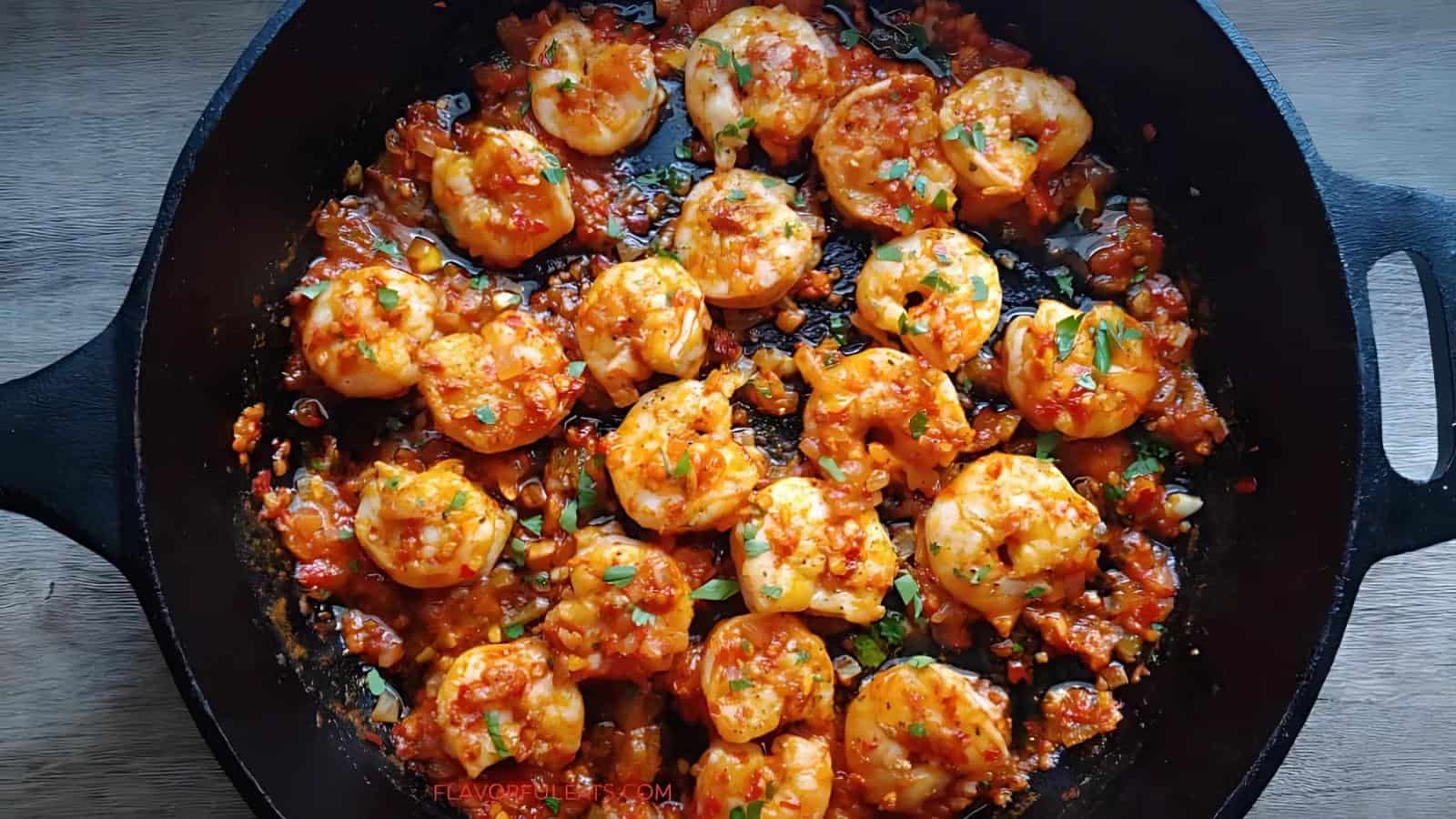 Shrimp cooked in a tomato-based sauce with herbs, served in a black skillet on a wooden surface.