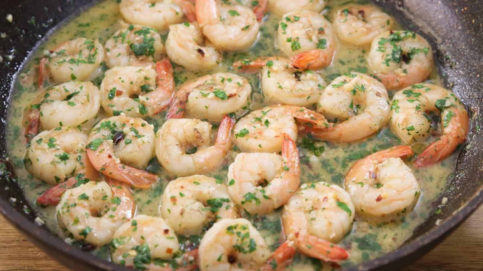 Shrimp cooked in a skillet with garlic, butter, herbs, and a light sauce, garnished with chopped parsley.