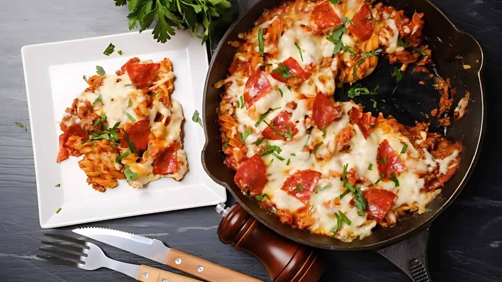 A cast iron skillet with baked pasta topped with melted cheese and pepperoni, next to a white plate with a serving of the dish, garnished with chopped parsley.