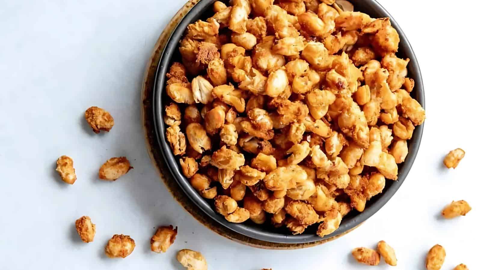 A bowl filled with crispy roasted chickpeas, with some scattered on a white surface around the bowl.