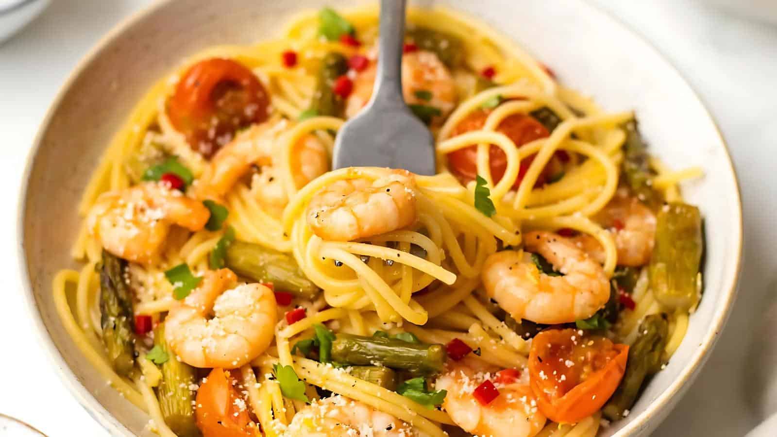 A bowl of spaghetti with shrimp, cherry tomatoes, asparagus, red chili, and grated cheese, with a fork twirling pasta in the center.