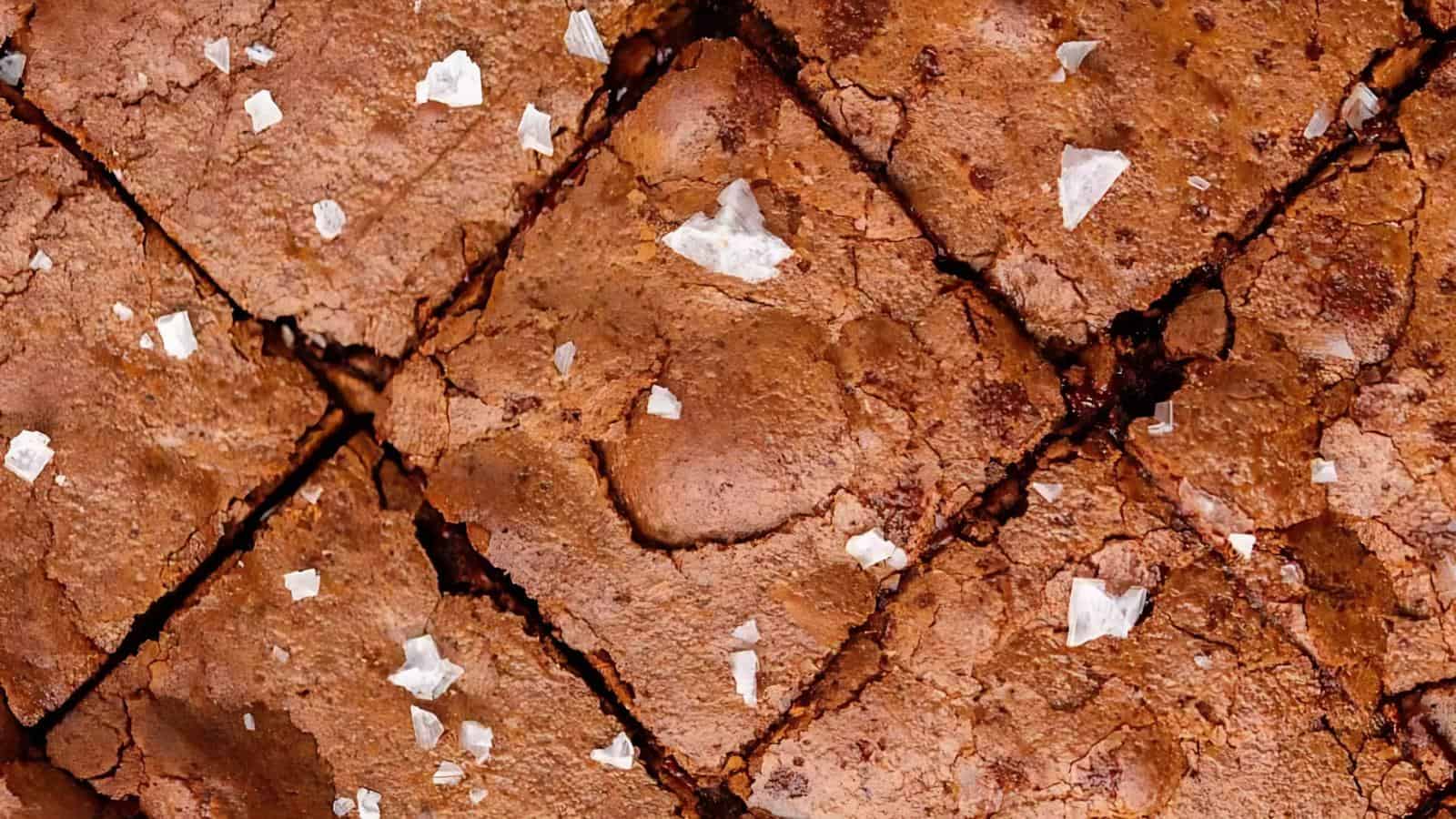 Close-up of sliced brownies with a cracked top, sprinkled with flaky sea salt.
