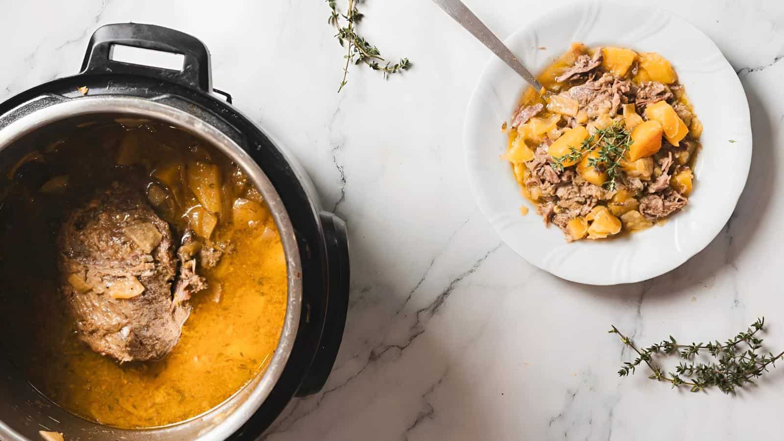 Cooked meat and potatoes in broth inside an Instant Pot, with a serving of the dish on a white plate garnished with fresh thyme on a marble countertop.