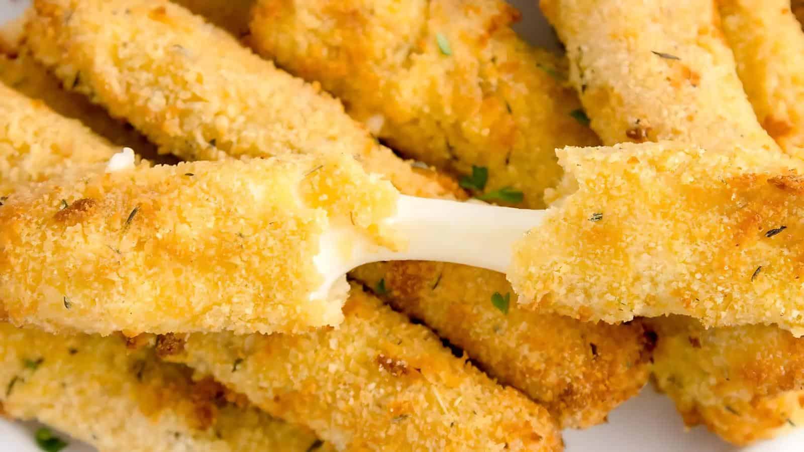 A close-up of breaded mozzarella sticks, with one being pulled apart to reveal melted cheese stretching between the halves.
