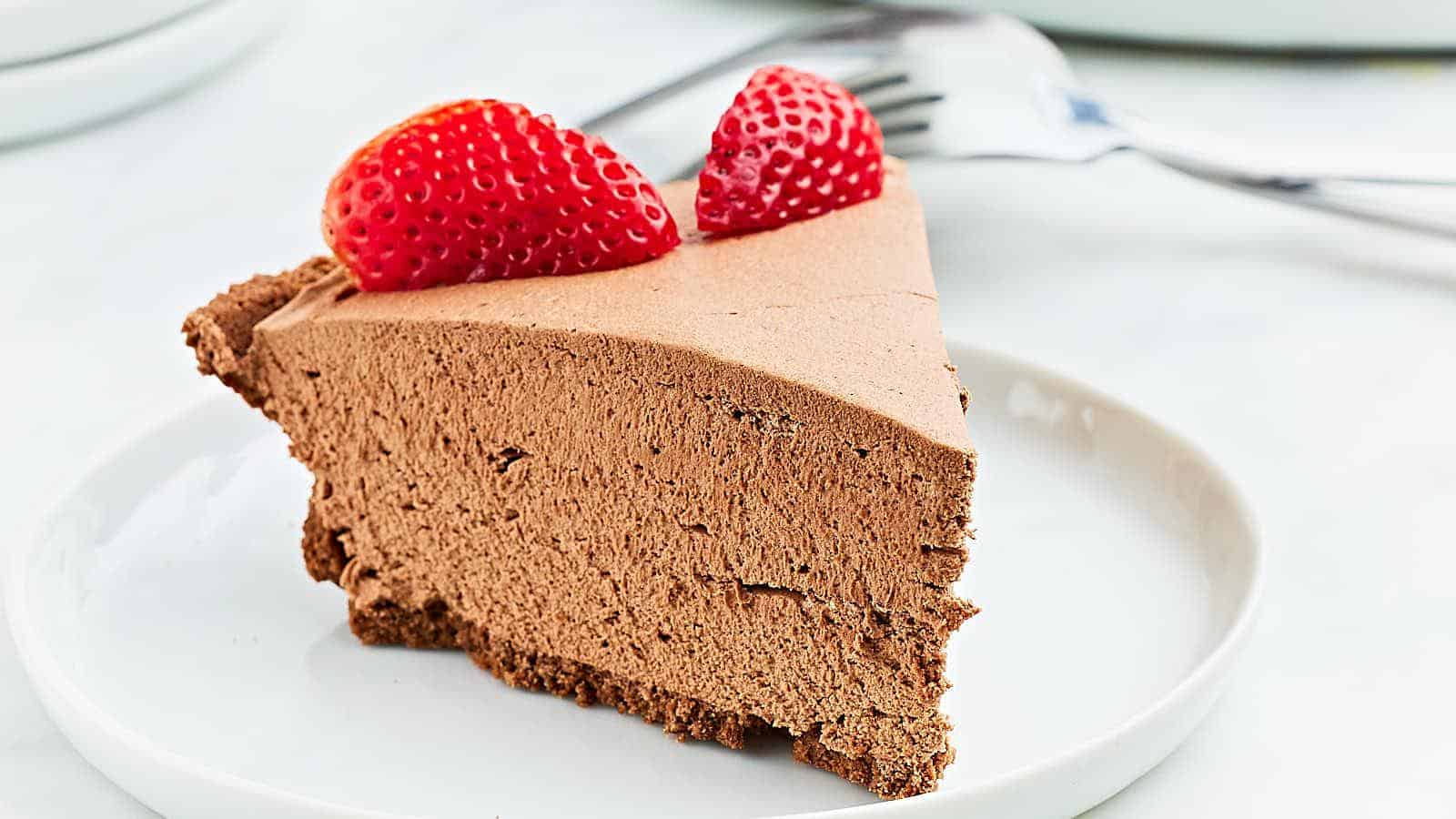 A slice of chocolate mousse pie topped with two strawberry halves on a white plate, with forks in the background.