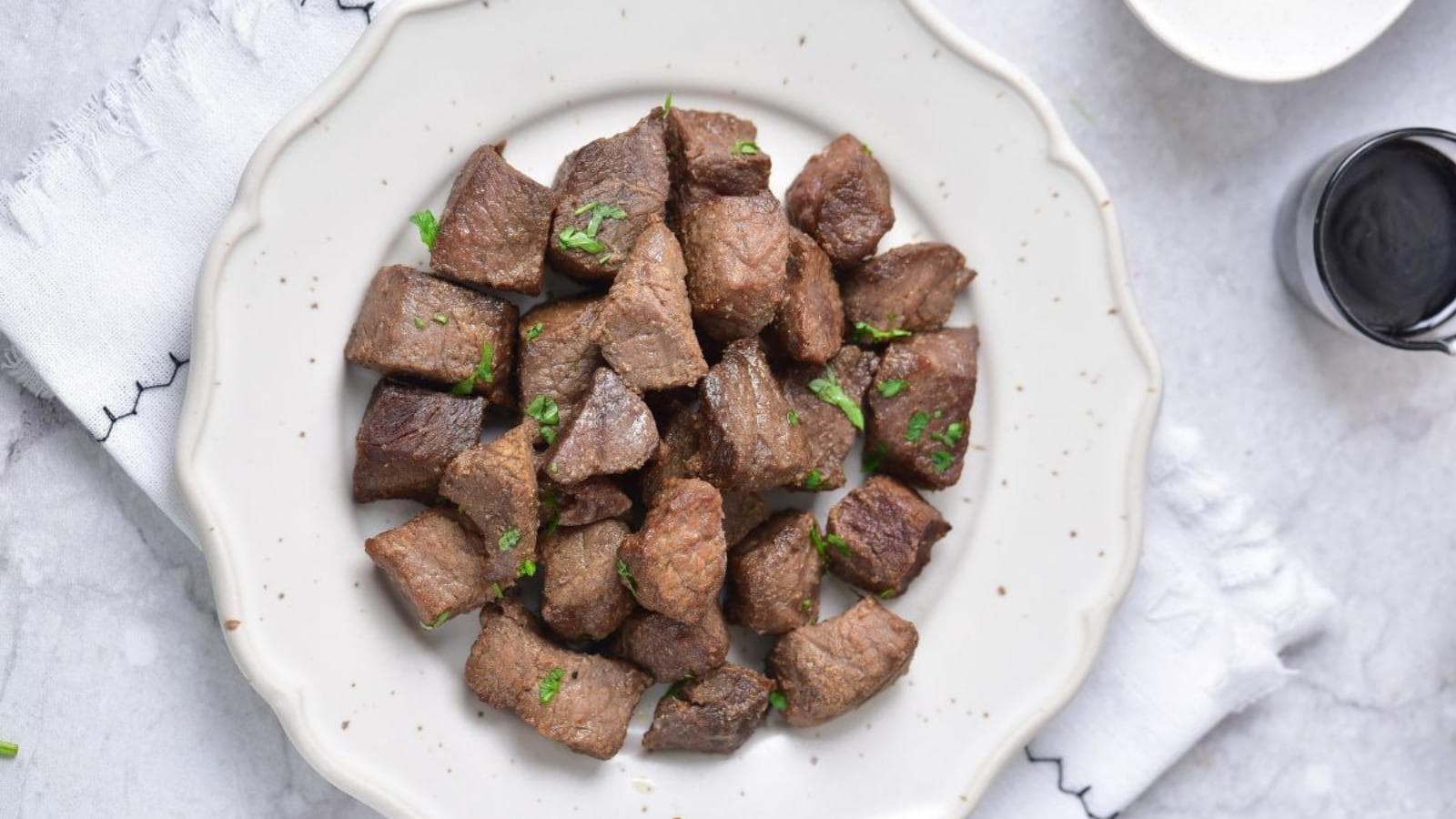 A white plate with cubed pieces of cooked beef garnished with chopped herbs.