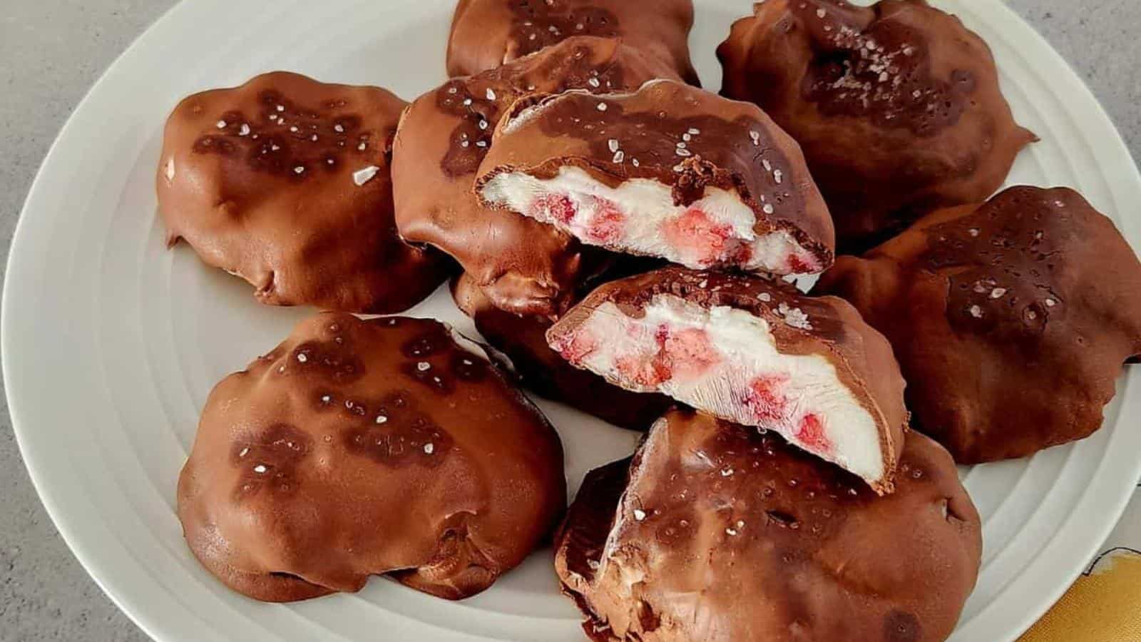 A plate of chocolate-covered clusters filled with marshmallow and bits of red fruit, some cut open to show the filling, sprinkled with coarse salt.