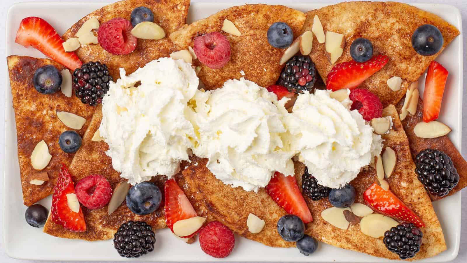 A plate of crepes topped with whipped cream, sliced strawberries, raspberries, blackberries, blueberries, and slivered almonds.