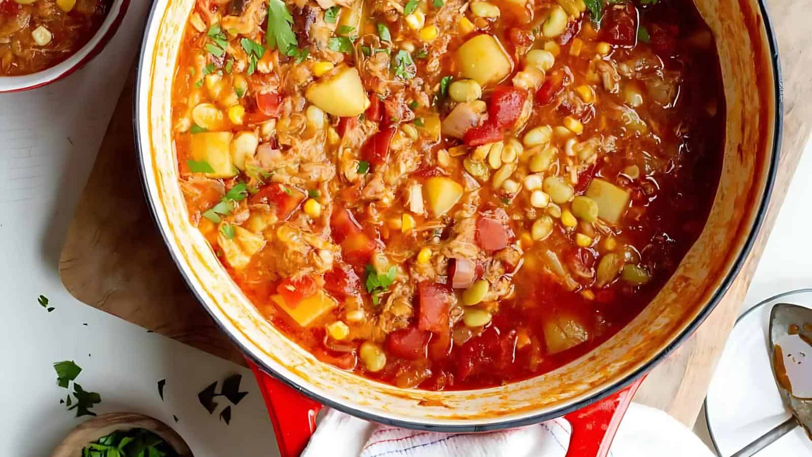 A pot of vegetable and meat stew with potatoes, corn, lima beans, and tomatoes, garnished with chopped parsley.