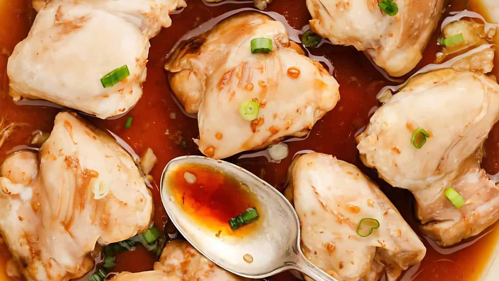 Pieces of cooked chicken in a brown sauce, garnished with chopped green onions, with a spoon resting in the sauce.