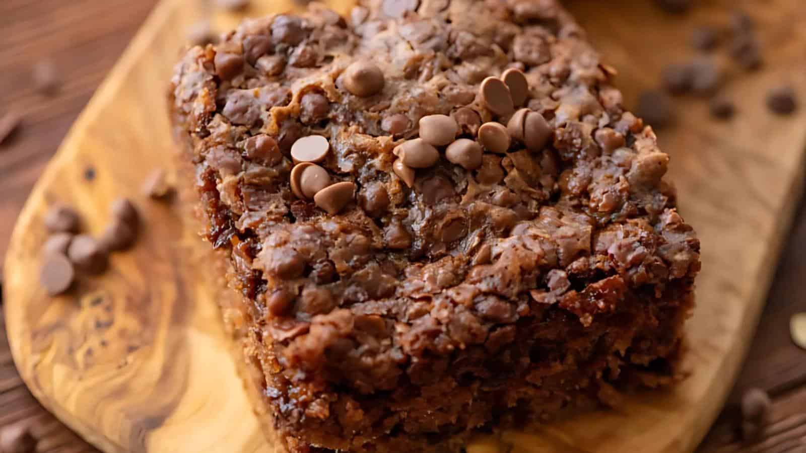 A close-up of a thick, rectangular slice of chocolate chip oatmeal cake on a wooden board, topped with chocolate chips.